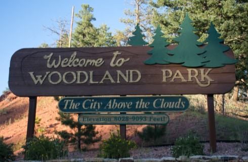 Large brown wooden sign with green pine trees saying Welcome to Woodland Park
