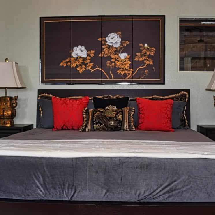 Bedroom with black wooden furniture, dark gray bedding, gray and red pillows, and large artwork hanging on the wall over the bed