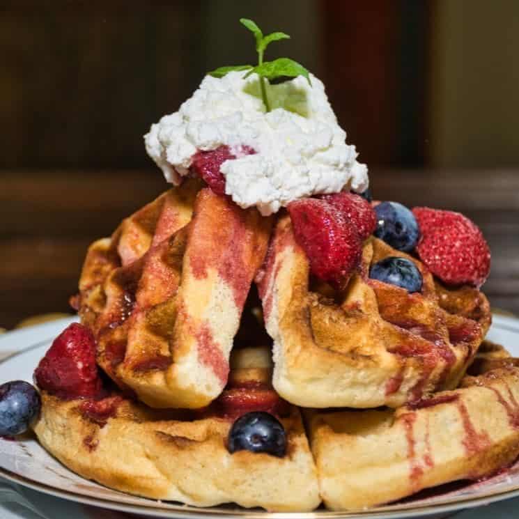 Close up view of waffles covered with strawberries, blueberries, whipped cream, and mint sprig on top