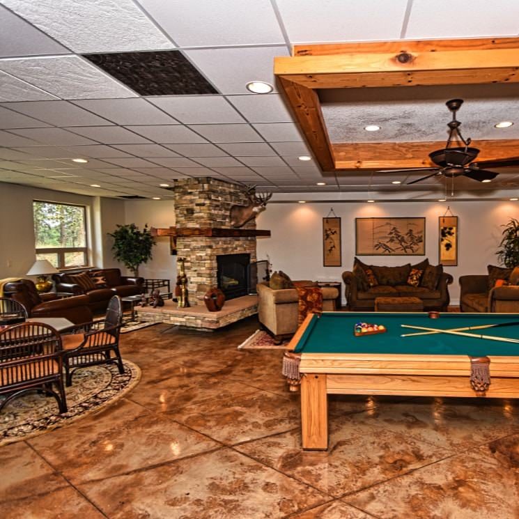 Large room with stamped concrete floor, multiple sofas and chairs, stone fireplace, wooden pool table, and a dining area